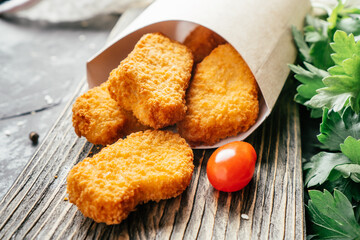Serving of chicken nuggets in craft paper bag with sesame seeds, cherry tomatoes, parsley on wooden surface