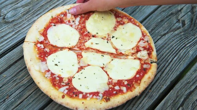 Female woman hand holding taking slice piece of fresh crust whole small pizza on table with melted mozzarella cheese and sprinkles and red tomato sauce closeup as Italian food cuisine