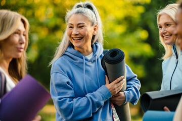 Multiracial women talking and smiling after yoga practice in park