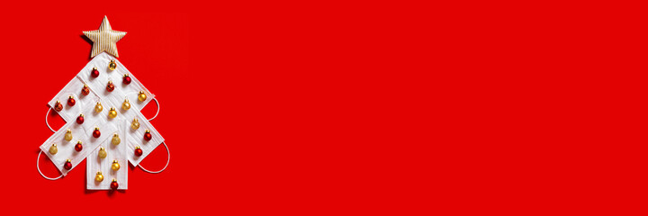 Creative Christmas tree made of white disposable medical masks with small Christmas red and golden balls, red colored banner with copy space. New year layout