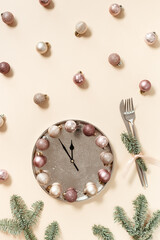 Winter festive table setting concept, Christmas plate with clock hands show twelve or midnight, sparkle balls beige pink color, knife, fork, fir tree branches. New Year holiday food concept
