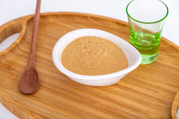 pot of Peruvian Maca powder under a bamboo tray, selective focus, on white background.