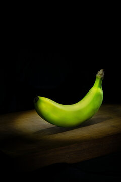 Green banana on wooden board on black background