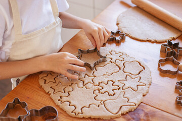 Children with their mother cut out Christmas gingerbread cookies on the table from rolled dough.