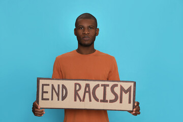 African American man holding sign with phrase End Racism on light blue background