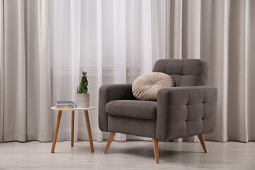 Comfortable armchair and plant near window in living room. Interior design