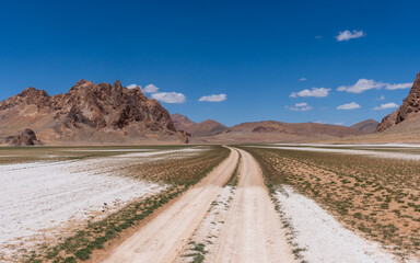 Endless gravel road cutting through the vast landscapes of the Pamir Highway in Tajikistan, surrounded by rugged, arid terrain