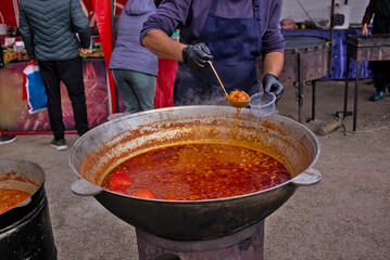 A ladle of Ukrainian borscht. Big cauldron with the Ukrainian national dish. The cook puts a portion of the traditional borscht into the container. Street food fair, event, festival. Ukraine.