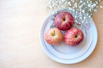 beautiful apples inside a white dish on top of a clear table with white flowers around