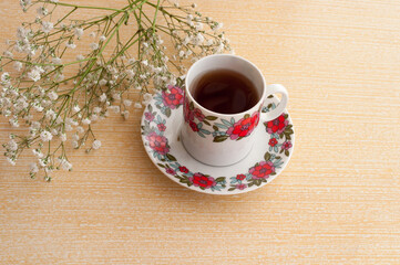 cup of coffee on top of a clear wooden table with white flowers round
