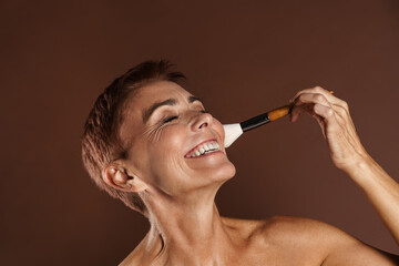 Obraz premium Senior shirtless woman smiling while using powder brush