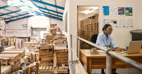 Young African woman using a laptop at her warehouse desk