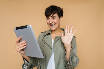 Mature european woman waving hand while using tablet computer