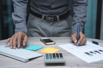 business man working on table at office. man hand use pen pointing on business graph or chart with keyboard, smartphone and tablet to analysis statistics and strategy for investment success target.