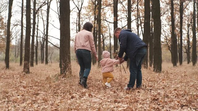 Happy family with little daughter walking in an autumn park in forest. Fun kid life with father and mother