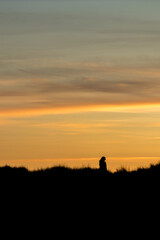 Silhouette of unrecognizable person at sunset with colorful layered sky above, vertical frame