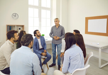 Group of people having serious business meeting in office. Senior man stands up while talking to team of colleagues. Corporate leader sharing advice and providing professional guidance for employees