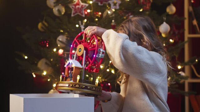 Little girl opening present box, taking toy, sitting on floor in decorated living room. Small child unpacking gift, surprised kid. Christmas holidays. New year atmosphere, happy childhood.