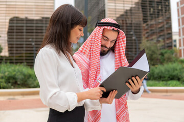 Young smiling caucasian businesswoman showing contract details to Arab man client before singing