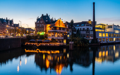 A cityscape at night with buildings illuminated and reflected in the water. The image captures the vibrant lights of the city, creating a stunning and serene atmosphere.