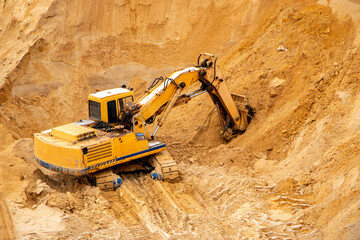 Obraz premium large yellow hydraulic industrial excavator, iron bucket miners, digging and loading sand, inside development of large sandy career.