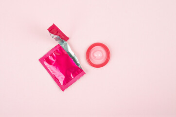 Pink opened condom unpack on a pink background.
