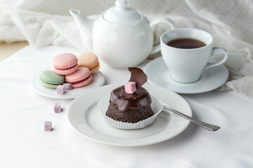 Obraz na płótnie Canvas Chocolate mini cake with glaze and macaroons and cup of tea on the table
