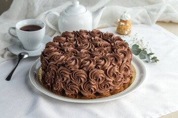 homemade glazed cake decorated with chocolate cream roses and cup of tea on the table