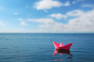 Pink paper boat floating on calm sea. Space for text