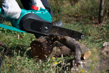 A man is sawing wood with an electric chain saw. Shavings fly out from under the saw links. 