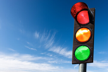 Closeup of a traffic light on a blue sky with clouds and copy space, with all three lights on,...