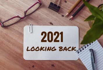 2021 looking back text on white card on office desk. Year highlights concept. Top view.