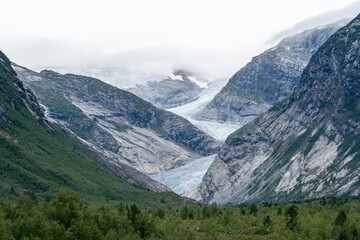 Glacier winding through a dramatic mountain valley in Norway, with mist rolling in.