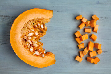 Fresh organic pumpkin slice and diced on a light blue wooden table.