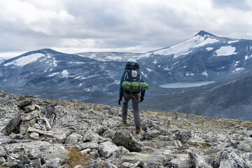 Hiker with backpack standing on rocky ground in Norway, taking in the vast mountainous view.