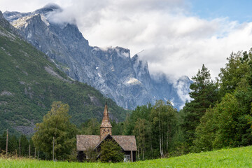 Traditional Norwegian stave church set against a mountainous backdrop in a lush valley.