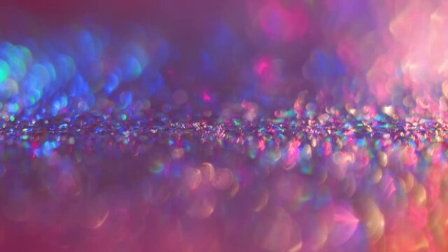Colorful spinning glitters rotating on the background with macro bokeh effect. Abstract blue, pink and violet purple decoration with shining and glowing multicolored particles. Holiday frame design.