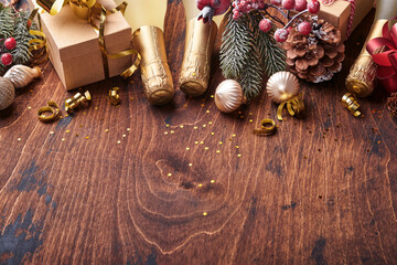 Christmas fir tree branches, champagne, Christmas balls, gift box, golden ribbons and stars on old wooden background for your xmas greetings. Top view with copy space. Christmas greeting card.