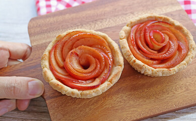 Hand Holding a Breadboard of Two Fresh Baked Mini Apple Rose Shaped Tartlets