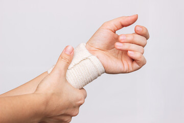 Cropped shot of a young woman holding a bandaged wrist in her hand isolated on a gray background....