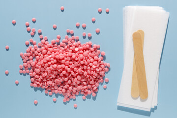 Beautiful pink depilatory wax granules, strips for depilation and wooden spatulas on a blue background. Epilation, depilation, unwanted hair removal. Top view.