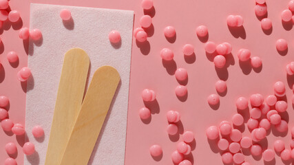 Beautiful pink depilatory wax granules, strip for depilation and wooden spatulas on a pink background. Epilation, depilation, unwanted hair removal. Top view.