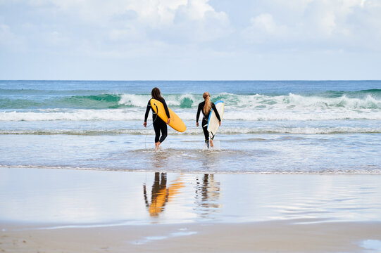 Couple of surfers with surfboards walking towards sea waves