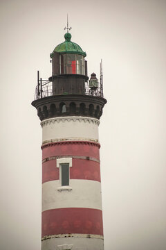 Red and white lighthouse on the rocky seashore. Vertical image. Maritime safety concept.