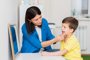 Woman speech therapist helps a child correct the violation of his speech in her office