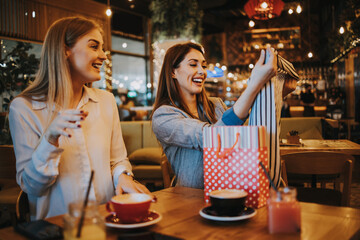Two best friends sitting in coffee bar or restaurant after shopping and happily talking together. They also show each other the clothes they bought.