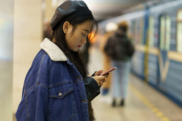 Dependent from smartphone asian girl pay no attention on arriving train on subway platform scroll...
