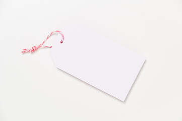 Blank gift tag with pink striped ribbon against white background. Top view, flat lay, copy space.