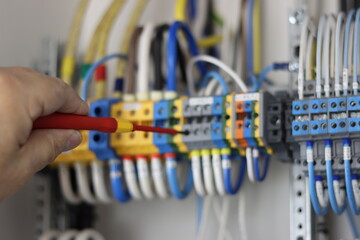An electrical engineer uses an insulated screwdriver to connect the equipment in the control panel