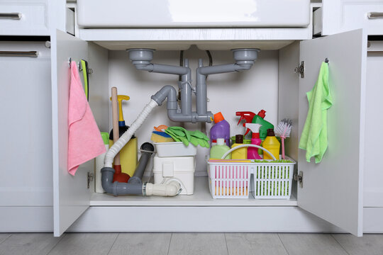 Open under sink cabinet with different cleaning supplies in kitchen
